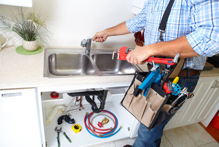 A plumber holds a wrench and checks a sink